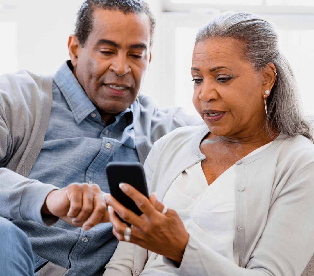 Older couple sitting on couch, woman holding smartphone while man points at the screen, both focused on the device