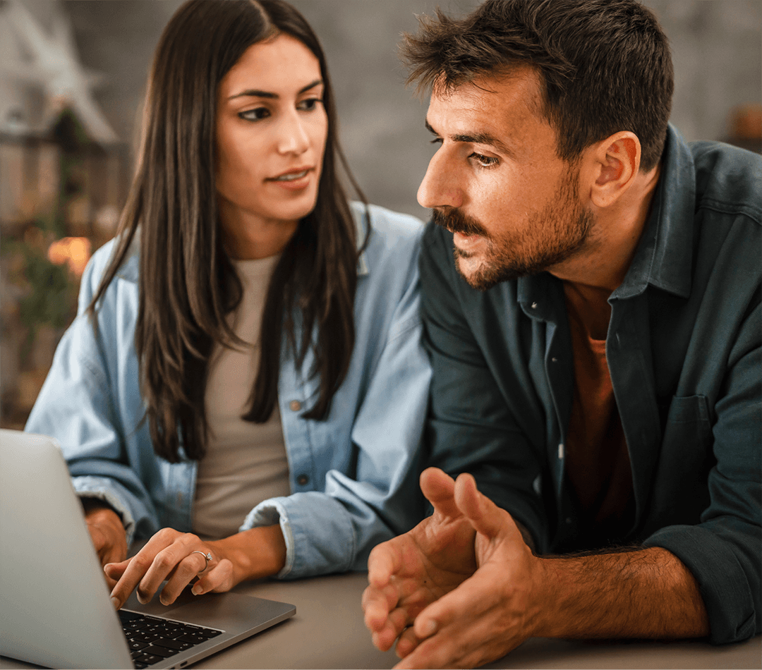 Two people sitting at a table working together on a laptop in a casual indoor setting