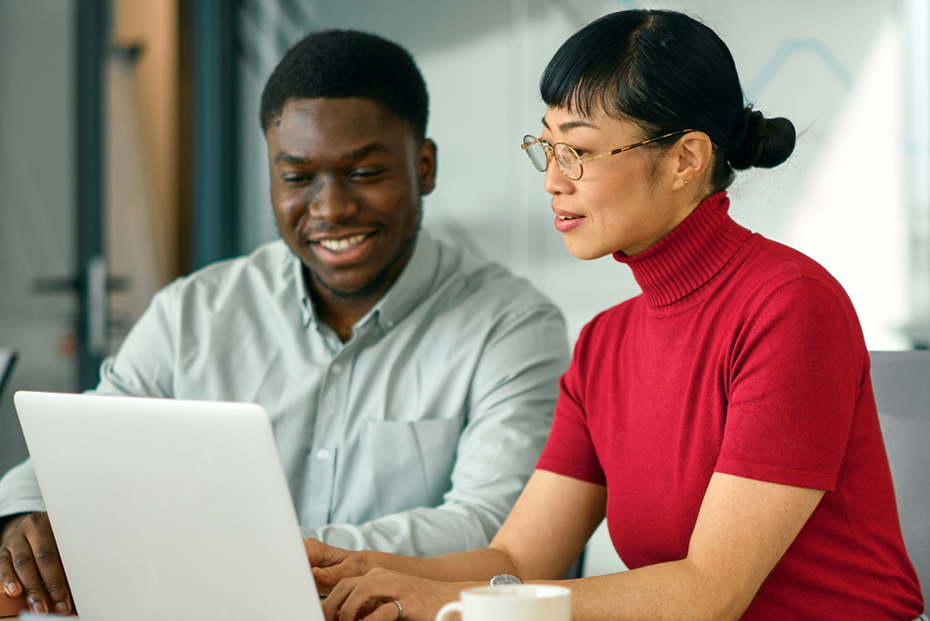 Two professionals collaborating on a laptop in a modern office meeting space, discussing work and digital business solutions.